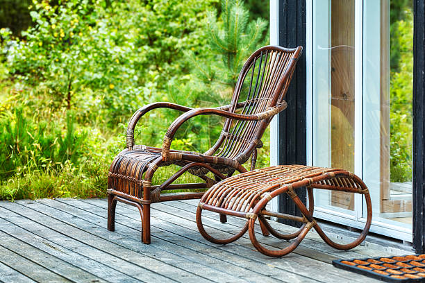 A cozy, elegant rattan chair with leg rest situated on a wooden deck overlooking lush greenery, perfect for enjoying outdoor leisure and relaxing moments in nature.