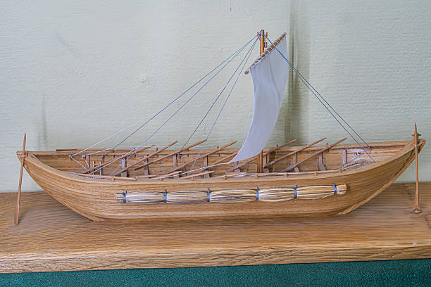 Ancient galley model wood, multiple masts, square sails, oars, flat bottom hull, intricate details rigging, oarlocks, textured surface, wooden stand, angled perspective