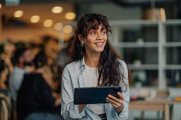 istock Young businesswoman using digital tablet, smiling and looking away in modern office 2227295526