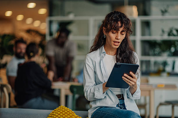 istock Focused businesswoman using digital tablet in modern office with colleagues working in background 2227295527