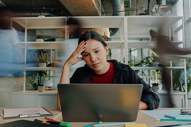 istock Stressed young woman working on laptop in busy office 2227295584