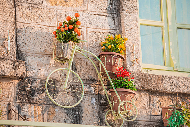 Decorative metal bicycle with flower pots hanging on a stone wall next to a window, creating a charming and picturesque scene