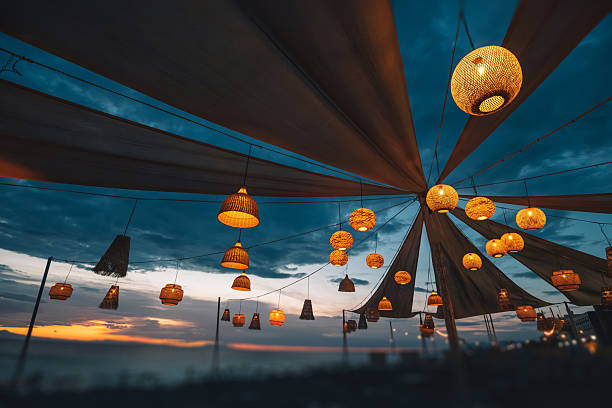 Warm light from hanging lanterns creates a magical atmosphere at an outdoor evening in beach bar, enhancing the vibrant sunset