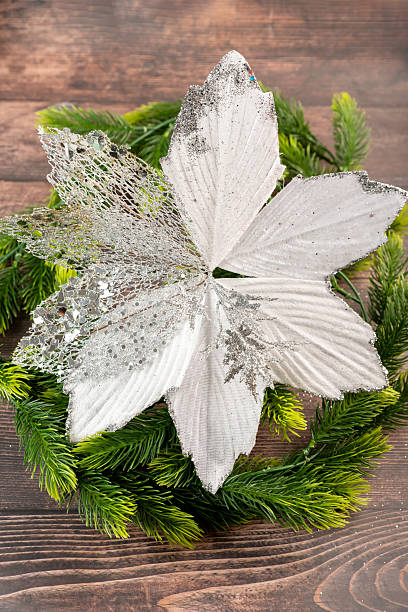 Glittering handmade Christmas flower with silver sparkles, placed on green pine branches. Ideal for New Year decor and winter-themed crafts.