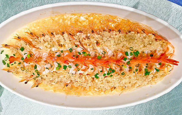 A visually striking dish of steamed prawns, arranged in two rows, topped with copious minced garlic and chives