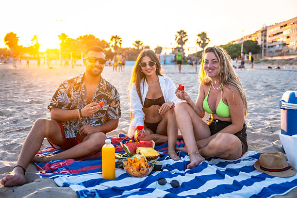 istock Friends eating watermelon and fruit at beach picnic during sunset 2227322935