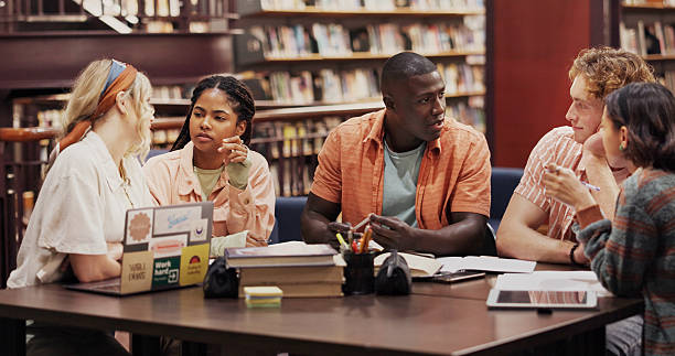 istock University, group and study with students or friends in library for research project, education and learning. Future, knowledge and college assignment with people and discussion for scholarship 2227323009