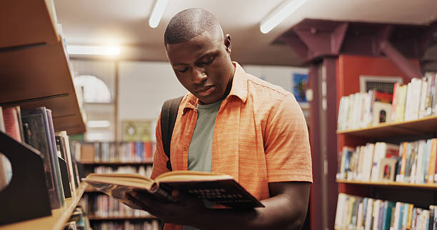 istock Black man, reading and book as student in library for research, studying and exam preparation. Person, novel and literature information for knowledge, education and language assessment at university 2227323031