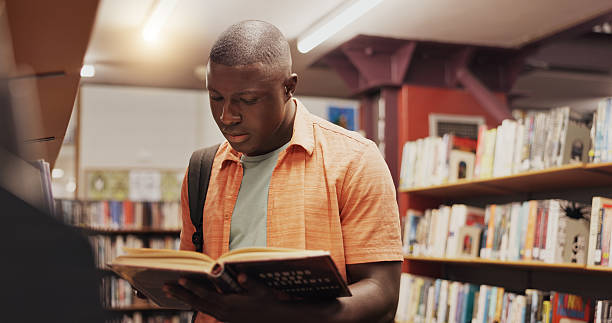 istock Black student, reading and book as man in library for research, studying and exam preparation. Person, novel and literature information for knowledge, education and language assessment at university 2227323033