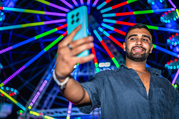istock Young man taking a selfie in front of ferris wheel at night 2227323766