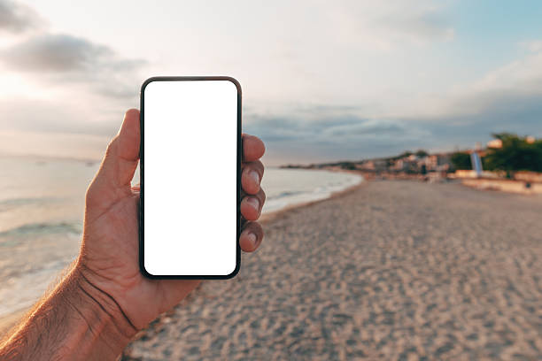 istock Hand holding smartphone with blank white screen on sandy beach at sunset, mockup or app presentation. 2227324072