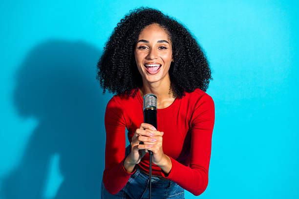 istock Young woman with a microphone poses confidently against a blue background 2227325382