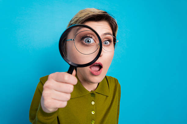 istock Young female professional holding a magnifying glass with a surprised expression against a solid blue background 2227327645
