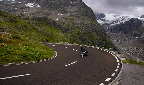 istock An alpine road with a sharp curve and motorcycle driver 2227334947