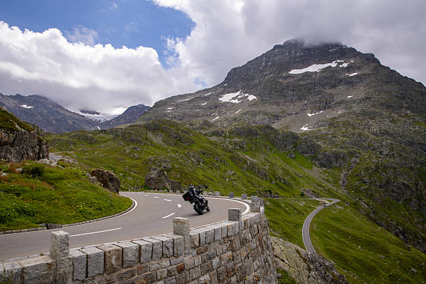 istock An alpine road with a sharp curve and motorcycle driver 2227334998
