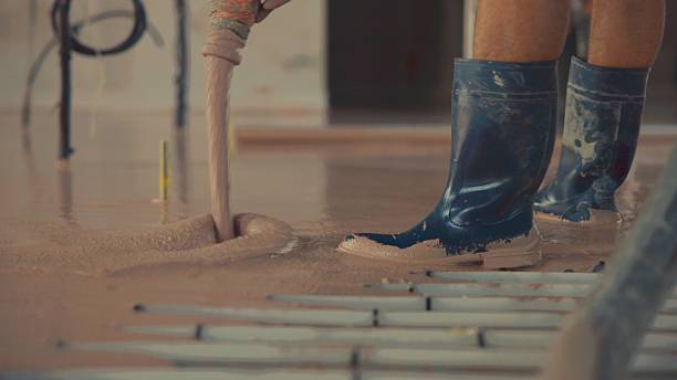 Construction worker pouring self-leveling anhydrite gypsum screed, covering underfloor heating pipes