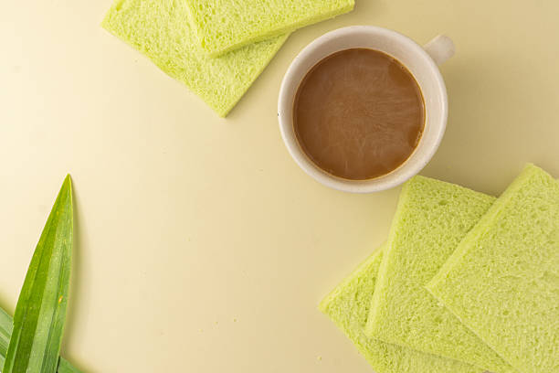 Soft pandan flavored bread with pastel green color, crustless, served with a warm cup of milk coffee. A cozy and simple breakfast or snack scene