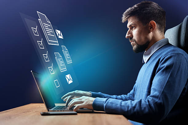 Professional man working on a laptop at home while interacting with floating digital documents in a modern workspace setting