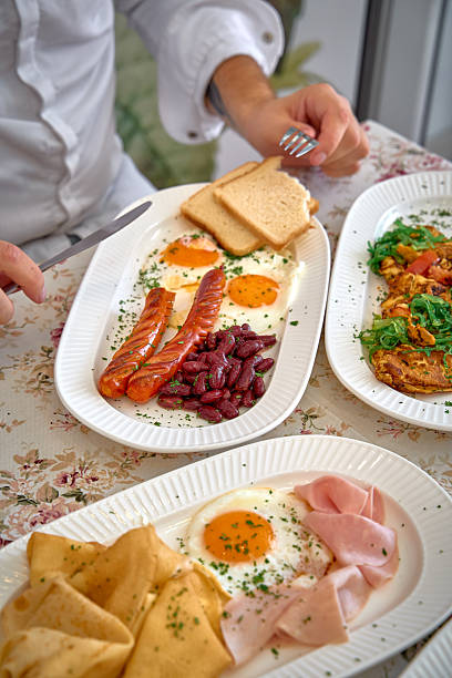 A Delectable Breakfast Spread Featuring Eggs, Sausages, Kidney Beans, Ham, and Crepes on a Floral Tablecloth Setting for a Delightful Morning Meal