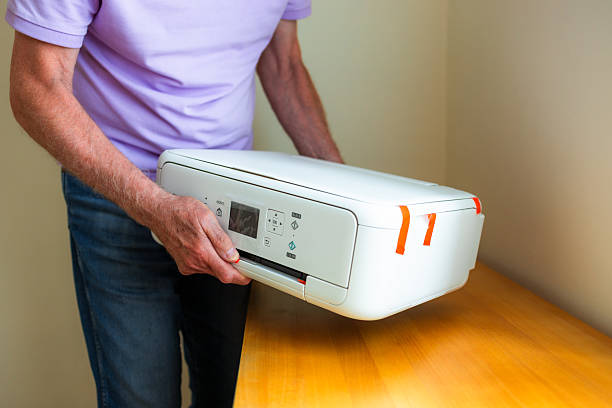 A senior man placing a new inkjet printer on the desk in his home office.