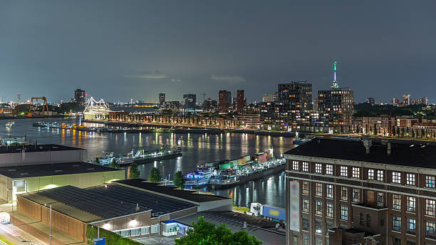 Aerial panoramic view over illuminated towers in Maashaven night timelapse with moored ships, Katendrecht and Maas River, Rotterdam. Traffic near former factory converted into office and event space