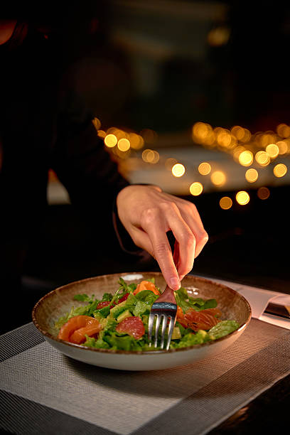 istock A Delicate Hand Reaching for a Colorful Salad, Highlighted by Warm Ambient Light and Multiple Fresh Ingredients in a Cozy Dining Setting 2227354021