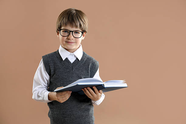 School boy of Indian ethnicity lying down on the floor at home and reading his text book portrait close up at home wearing school uniform.