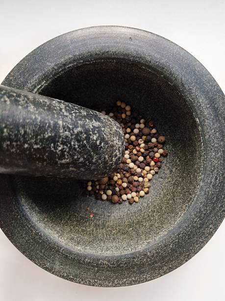 Close-up of granite mortar and pestle with a blend of black, white, red, and green peppercorns, ready for grinding.
