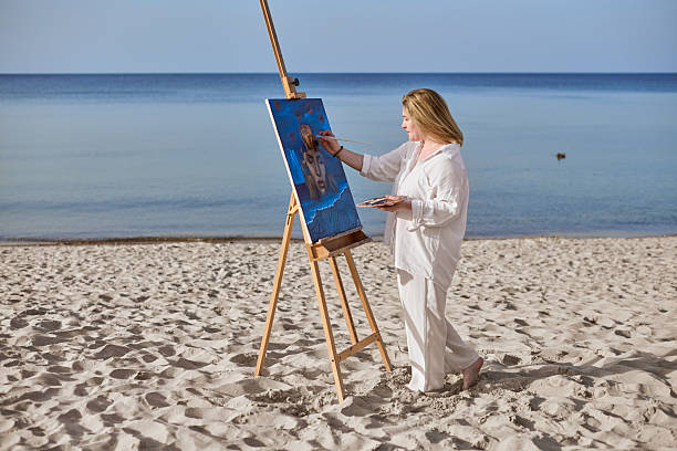 istock Young female artist painting on tranquil beach setting 2227354993