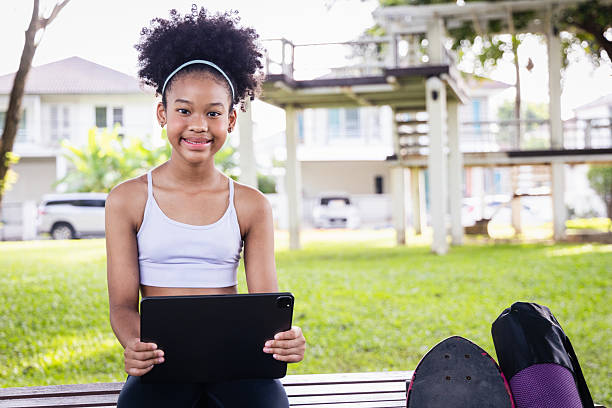 istock African American girl exercise outdoors holding tablet with skateboard and backpack on bench in park 2227355945