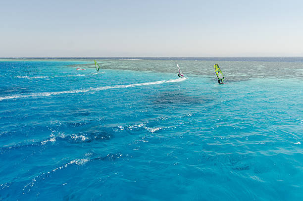 Windsurfer riding across turquoise waters under a bright blue sky, with sailboats in the distance. Shot in Naxos, Greece. Perfect summer sport and vacation concept.