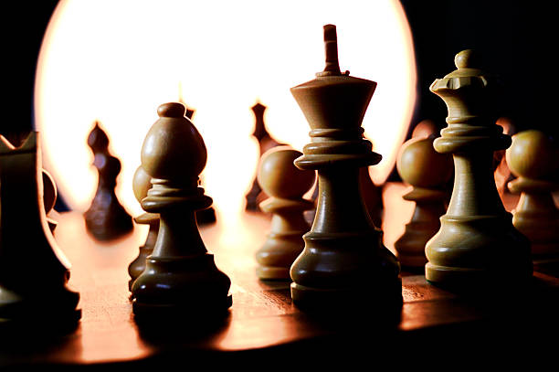 istock Horizontal side view of black colored illuminated chess pieces pawns, king, queen, bishop in silhouette against bright white light backdrop, for strength, power, teamwork, togetherness, intellectual force with copy space. Slight deliberate grains 2227366992