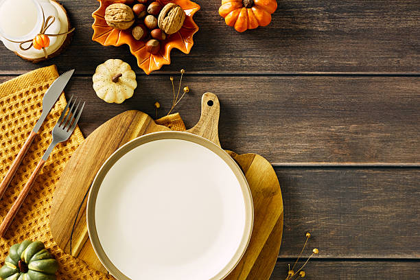 istock Autumn table setting with white plate on wooden cutting board, yellow cloth, nuts, ceramic candle holder, and decorative pumpkins 2227368615