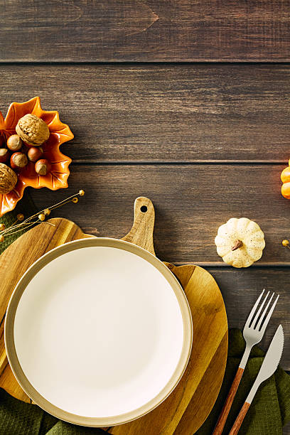 istock Autumn table setting with white plate on wooden board, green cloth, orange leaf-shaped bowl filled with nuts, rustic cutlery, and decorative pumpkins. Cozy fall composition ideal for Thanksgiving or seasonal dining 2227368703