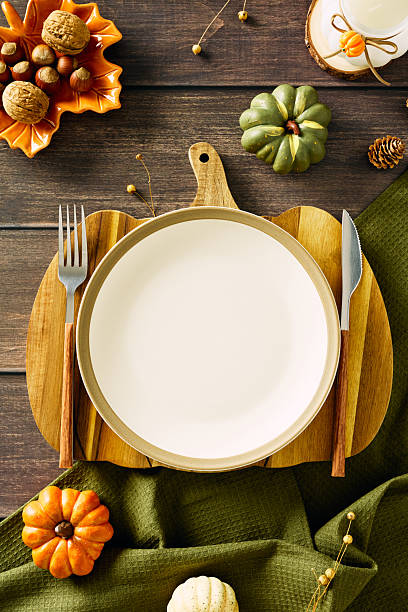 istock Elegant autumn table setting with white plate on pumpkin-shaped board, leaf-shaped orange bowl with nuts, rustic cutlery, green pumpkin, candle wrapped with twine, and pinecone accents 2227368742