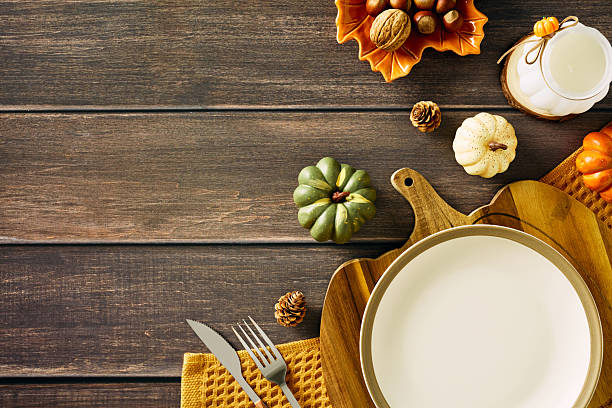 istock Rustic autumn table setting with white plate on wooden cutting board, yellow napkin, decorative pumpkins, pinecones, and ceramic candle holder. Cozy fall arrangement ideal for festive dining visuals or Thanksgiving themes. 2227368867