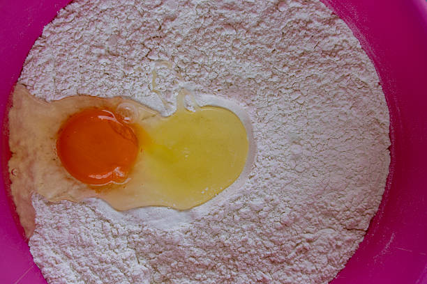 Top view of a pink mixing bowl filled with flour and a cracked egg yolk.  Baking ingredients prepared for making dough or pastry. Homemade cooking scene in a minimalist kitchen setting.