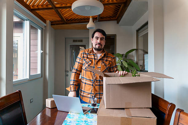 istock Man unpacking boxes and using laptop in new home office 2227371359