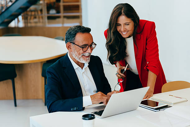 istock Two senior professionals discussing work at a desk with a laptop 2227376930