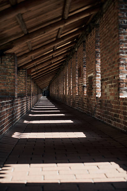 Brick corridor inside Nizhny Novgorod kremlin bathed in sunlight. Shadows create dynamic patterns on brick floor. Perspective leads towards vanishing point