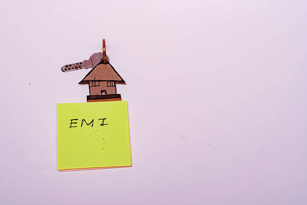 Close-up of a handmade car-shaped keychain with key and sticky note marked EMI, symbolizing financial burden, car loan repayment pressure, and personal finance challenges.