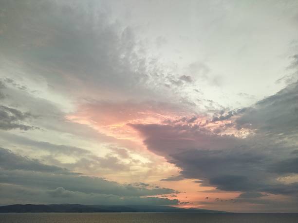 A breathtaking sunset scene featuring vibrant colors and dramatic cloud formations over a tranquil ocean. Soft hues of pink, orange, and purple blend seamlessly with the evening sky, reflecting gently on the water’s surface. The distant shoreline and layered clouds create depth, evoking a sense of serenity and wonder. Perfect for themes of nature’s beauty, peaceful moments, and scenic travel destinations.