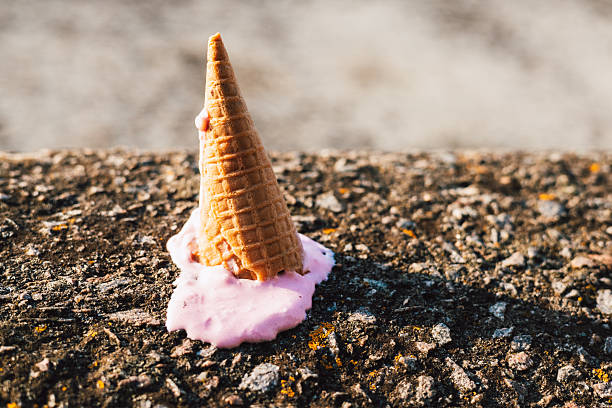 istock Fallen ice cream cone with spilled pink ice cream on a textured concrete surface. An ice cream cone, tipped over on a rough stone surface with spilled ice cream, and a blurred sea on the background. 2227397556