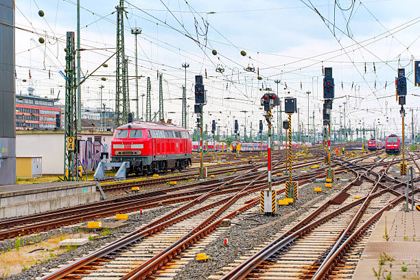 Frankfurt, Germany - June 10, 2025: Vibrant train yard in Frankfurt featuring a red locomotive, rail tracks, and numerous signals under a cloudy sky, illustrating urban transportation dynamics.