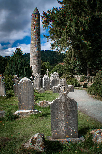 Glendalough Round Tower, County Wicklow, Ireland, tower rising above headstones, blue sky with scattered clouds.  Tower was built approximately 1,000 years ago.