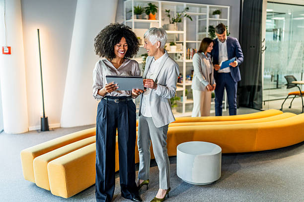 istock Businesswomen using digital tablet, smiling and discussing in modern office 2227403651