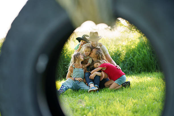 A family sits close in an embrace on a grassy lawn, surrounded by sunlight and greenery. A creative circular framing adds a unique perspective, emphasizing their love and connection in the outdoors.