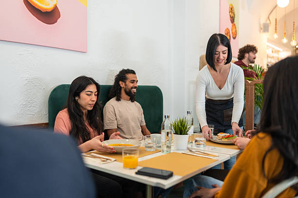 istock Friendly Waitress Serving Brunch to Diverse Group in Cozy Bistro with Bright Decor 2227404924
