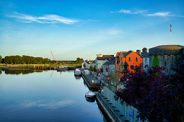 Scenic view of the River Corrib with colorful buildings and a stone fort in Galway, Ireland.
