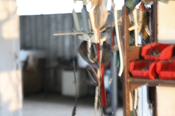 Softly Focused Image Of A Workshop Interior Featuring Hanging Tools, Wires, And Red Storage Bins. The Sunlight Illuminates The Space, Creating A Dreamlike Industrial Scene That Evokes Craftsmanship, Manual Work, And Everyday Repairs.